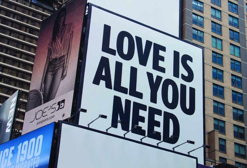 This image shows a billboard on the side of a building that says love is all you need.